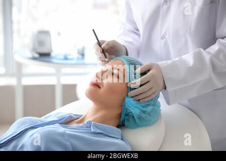 Plastic surgeon applying marks on woman's face in clinic Stock Photo