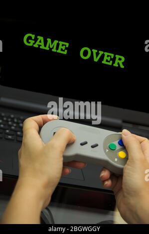 Close-up of a person playing with the gamepad on the computer with the words GAME OVER on the screen Stock Photo