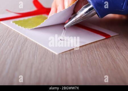 Woman's hand making postcard with red ribbon and bow with a help of glue gun Stock Photo