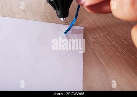 Woman's hand making postcard with blue ribbon with a help of glue gun Stock Photo