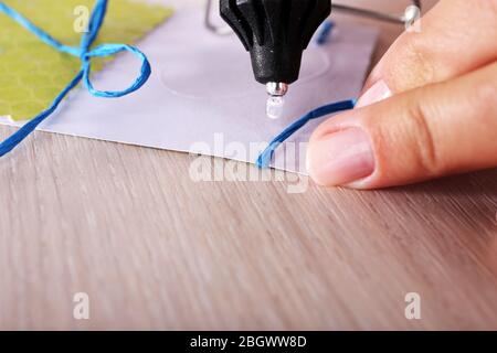 Woman's hand making postcard with blue ribbon and bow with a help of glue gun Stock Photo