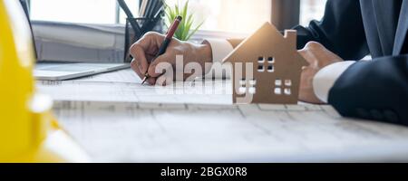 business engineer planing and checking on blueprint on table background of small model house, real estate concept Stock Photo