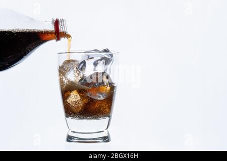 Cold drinking, pouring soda from bottle, glass of cola with ice for hot and summer drink isolated on white background Stock Photo