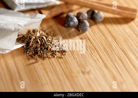 Close up of an open herbal tea bag with loose herbs and juniper berries and cinnamon sticks on a bamboo cutting board with shallow depth of field Stock Photo