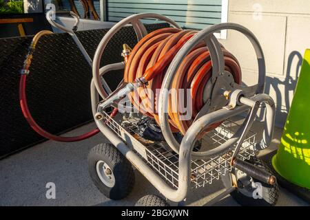 orange water hose rolled up on a Portable Garden Hose Reel Wagon Stock Photo