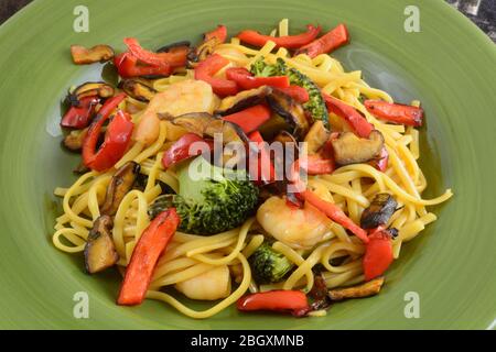 Close up of shrimp and pasta dinner with broccoli, red bell peppers, and shitaki mushrooms in green plate Stock Photo