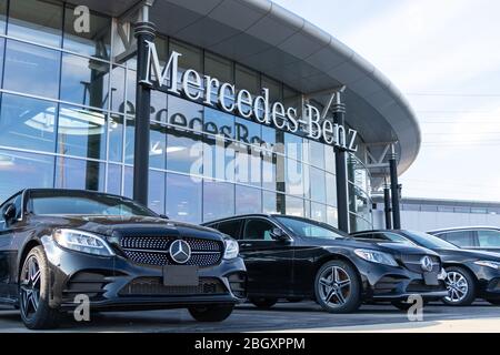 Mercedes-Benz text logo hanging at the front of a dealership with new cars parked in-front.