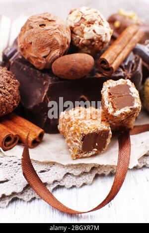 Pile of chunk of chocolate and truffles with cinnamon stick on crumbled paper, grey material and wooden background Stock Photo