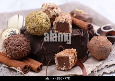 Pile of chunk of chocolate and truffles with cinnamon stick on crumbled paper, grey material and wooden background Stock Photo