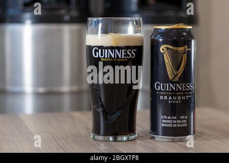 Guinness draught shout beer can on a table beside a full glass of beer in a Guinness glass with stacked kegs in the background. Stock Photo