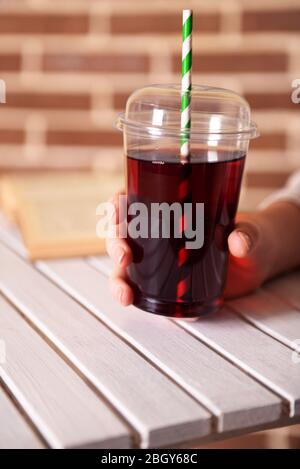 Female sitting at wooden table with fast food closed cup of pomegranate juice and near book on brick wall background Stock Photo