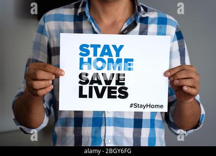 Man holding sign 'Stay Home Save Lifes' global message amid coronavirus crisis. Quarantine message across the globe to fight COVID-19 pandemic. Stock Photo