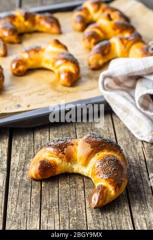Sweet homemade croissants with poppy on wooden table. Stock Photo