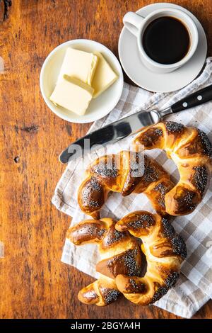 Sweet homemade croissants with poppy, butter and coffee on wooden table. Top view. Stock Photo