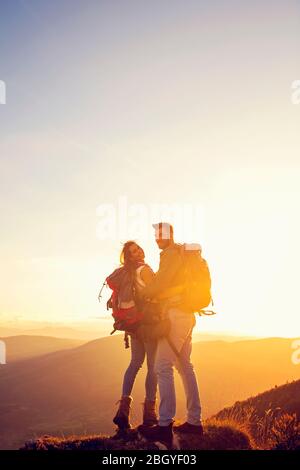 Hikers with backpacks relaxing on top of a mountain and enjoying the view of valley Stock Photo