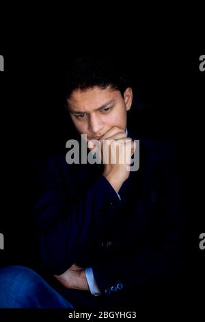 Portrait shot of confused thinking businessman/ceo/ executive wearing a blue colored suit with a black tie with one hand on his face near the chin and Stock Photo