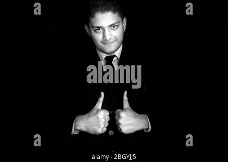 Happy and positive businessman wishing hope by raising thumbs of both the hands and gesture of hope/best isolated on a black background. Businessman w Stock Photo