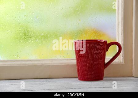 Cup of hot drink on windowsill on rain background Stock Photo