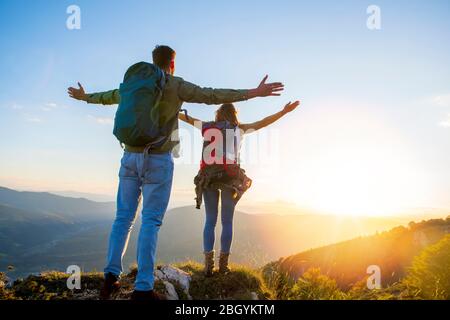 Couple with raised arms holding hands and looking at sunset Stock Photo