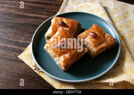 Baklava turkish sweets with walnuts and sirup., in green plate on wooden table, tea towel. Homemade dessert, bakery. Stock Photo