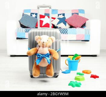 Suitcase with teddy bear and child toys in room on white sofa background Stock Photo
