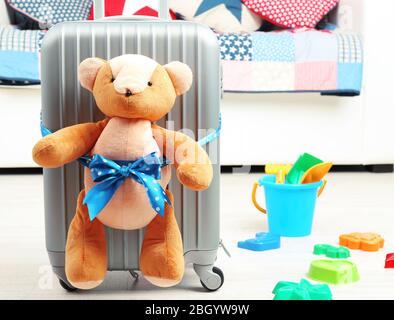 Suitcase with teddy bear and child toys in room on white sofa background Stock Photo