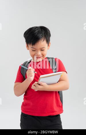 School boy with backpack writting something on his notebook, isolated on white. Stock Photo