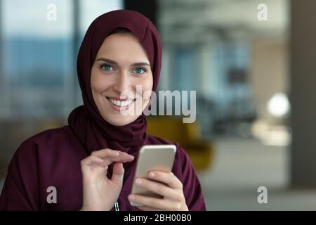 Happy muslim businesswoman in hijab at office workplace. Smiling Arabic woman working on laptop and talking on smartphone Stock Photo