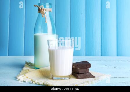 Glass and bottle of milk with chocolate chunks on color wooden planks background Stock Photo