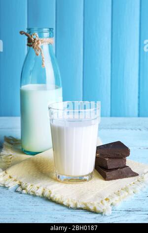 Glass and bottle of milk with chocolate chunks on color wooden planks background Stock Photo