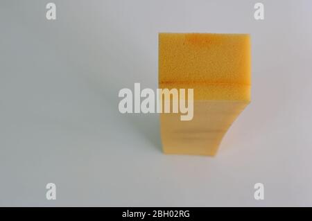 Closeup a piece of sponge standing in upright position on white wooden table, shallow depth of field, high angle view Stock Photo