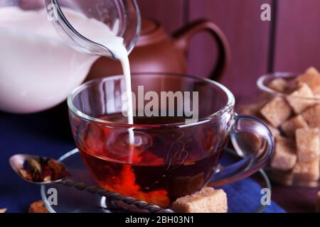 Pouring milk on tea and lump sugar and spices on color wooden planks background Stock Photo