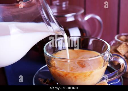 Pouring milk on tea and lump sugar and spices on color wooden planks background Stock Photo