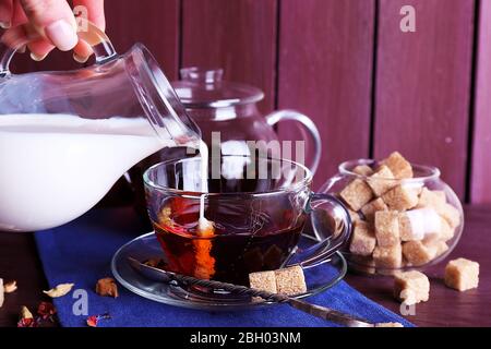 Pouring milk on tea and lump sugar and spices on color wooden planks background Stock Photo