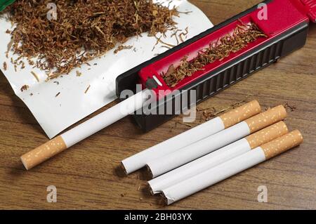 Cigarettes, tobacco and rolling machine on table Stock Photo