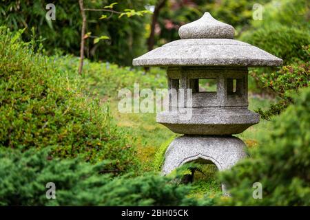 Close up of a stone japanese votive lantern, surrounded by green bushes and hedges at the Japanese Tea Garden in San Francisco Stock Photo