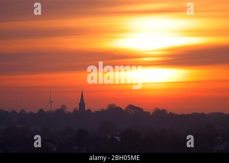 A beautiful sunrise over Garforth in Leeds. Hook Moor Wind Farm & St Mary's church stand out above the horizon Stock Photo