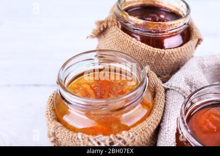 Homemade jars of fruits jam in burlap pouches on color wooden planks background Stock Photo