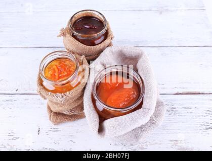 Homemade jars of fruits jam in burlap pouches on color wooden planks background Stock Photo