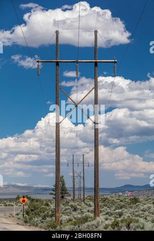 Symmetrical shot of a row of power line poles against a blue sky with puffy clouds in a desert landscape Stock Photo