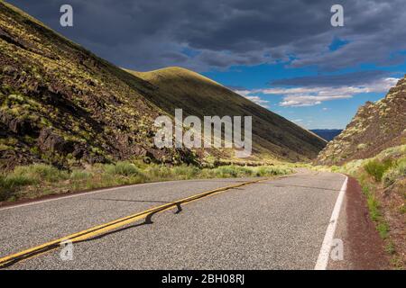 Low angle view of a remote country road snaking its way between hills in Nevada, under a blue summer sky with dark clouds Stock Photo