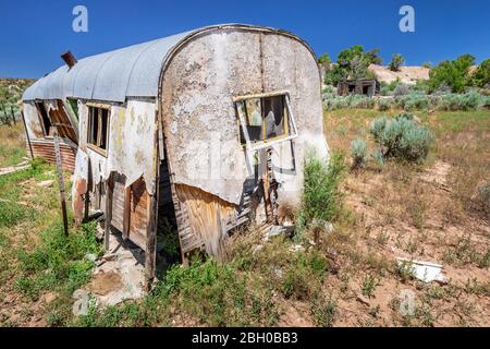 An old, abandoned trailer is falling apart in the american countryside; in the distance a log cabin is following a similar fate Stock Photo