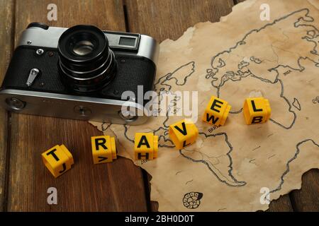 Retro camera on world map with word Travel on wooden table background