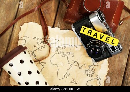 Retro camera on world map with word Travel on wooden table background