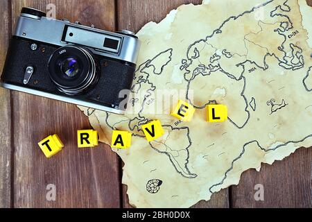 Retro camera on world map with word Travel on wooden table background