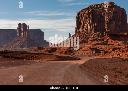 A dirt road snakes through the Monument Valley, with two huge red sandstone formations in the background Stock Photo