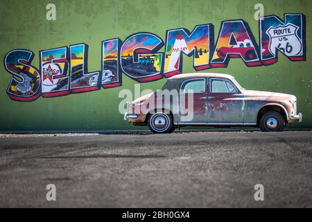 Close up of the Seligman logo painted on a green plaster wall, with a weathered red sedan car parked just below it Stock Photo