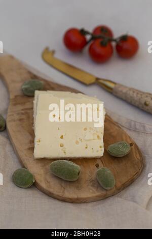 Slices of white cheese served on a wooden board with green almonds and cherry tomatoes. Vertical composition. Stock Photo