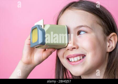 Child girl looks at old photos through a diascope. Banner template on pink background. Stock Photo