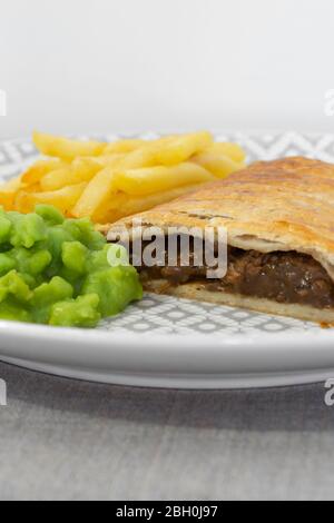 Steak and onion lattice pie with fries and mushy peas.  On a grey marl tablecloth Stock Photo